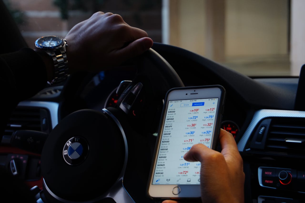 heros-img Person using mobile phone for currency trading while driving BMW car.